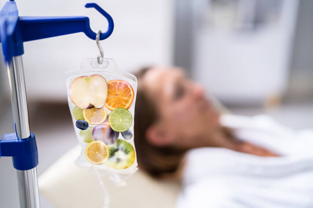 An IV bag of fruits full of vitamins with a woman laying down getting an IV drip.
