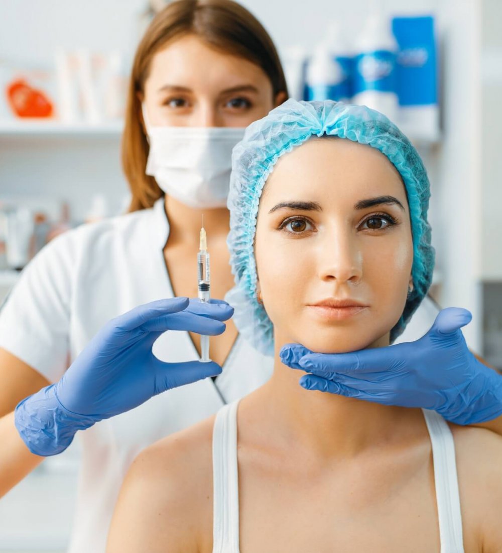 a woman in a chair getting botox and fillers on her face. Doctor wearing blue medical gloves touching her face.,